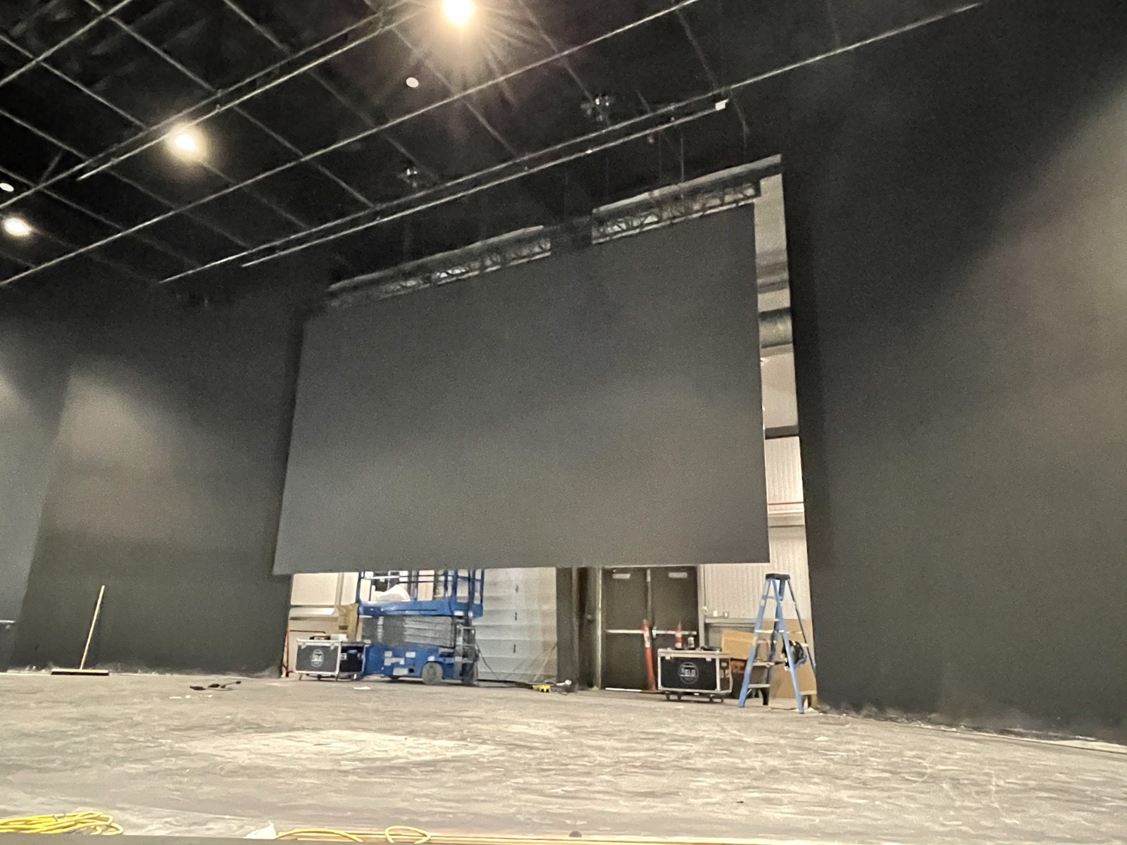Large-format LED video wall being installed in a large black-box venue with a lift and road cases
