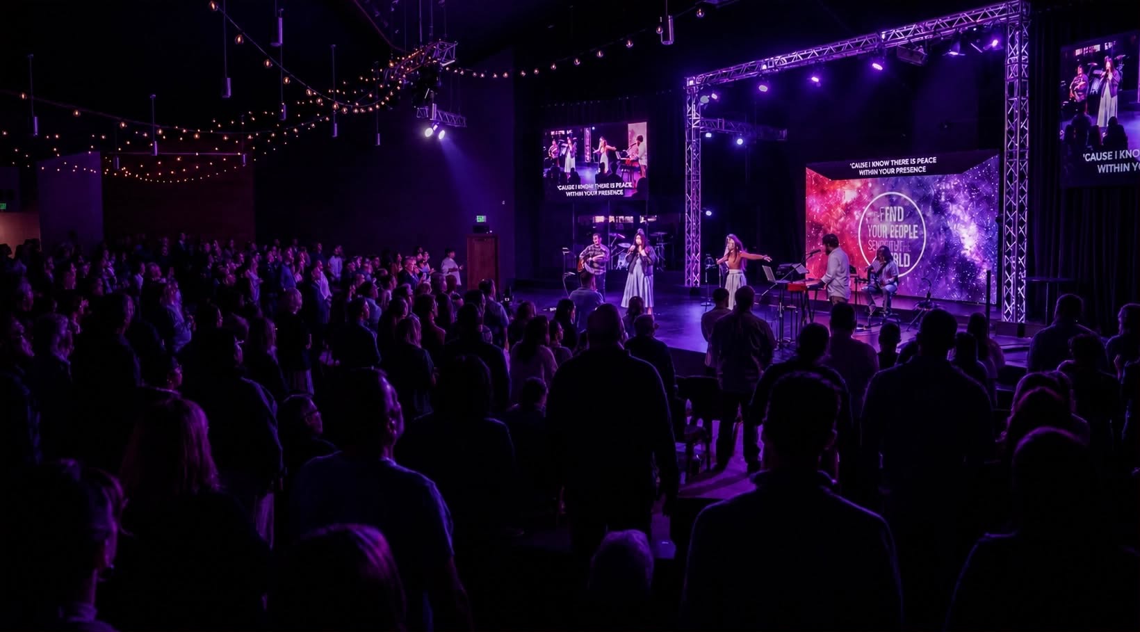 Packed worship service with a main LED video wall and IMAG side screens showing lyrics