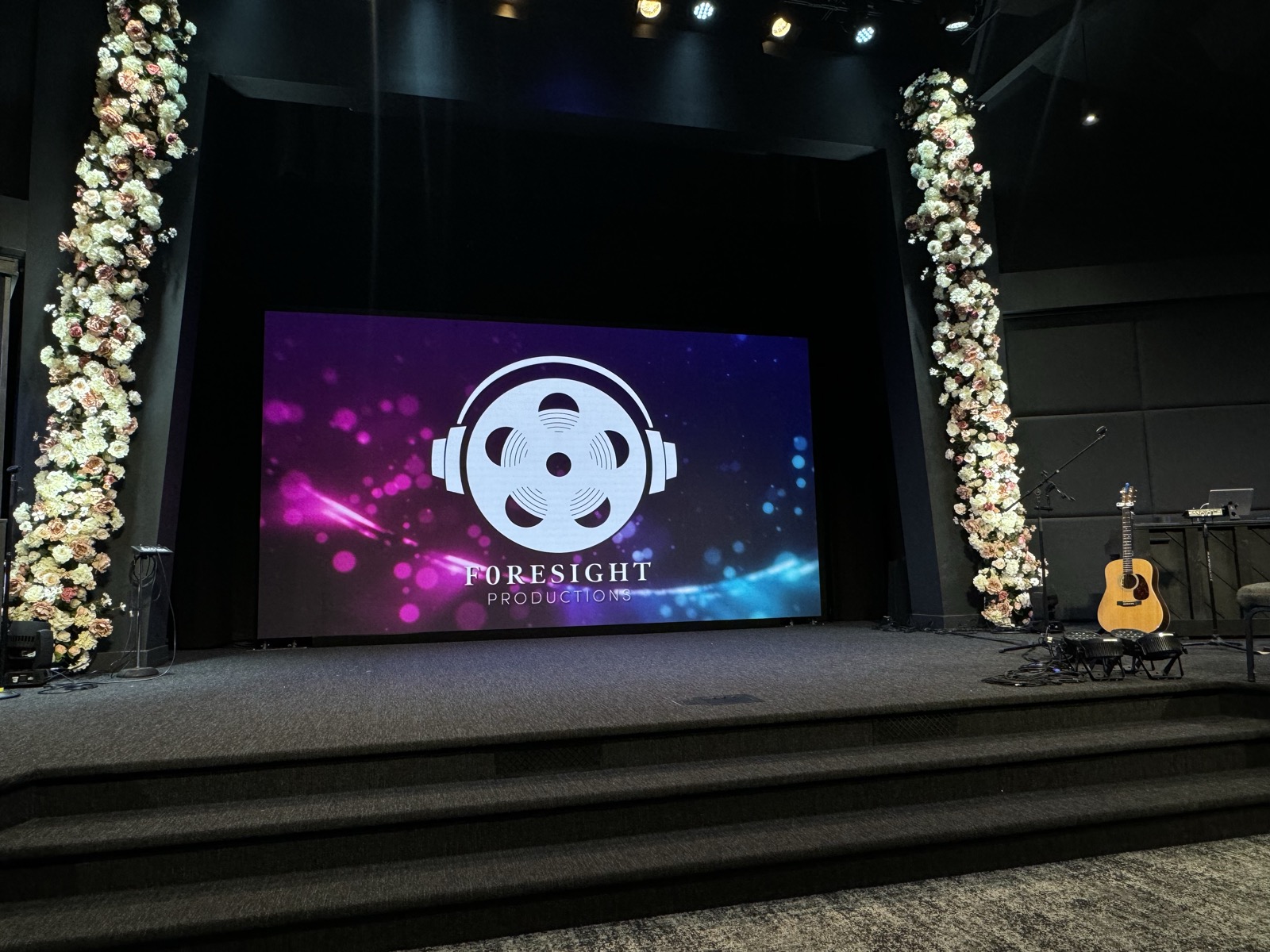 Church sanctuary stage with a large LED video wall flanked by floral arrangements